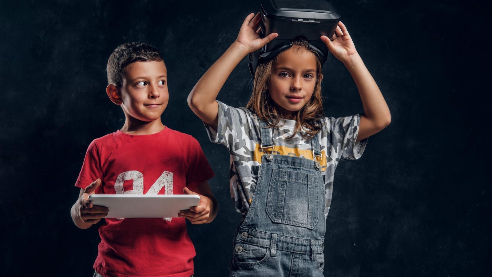 happy smiling boy is holding tablet while girl is wearing vr goggles