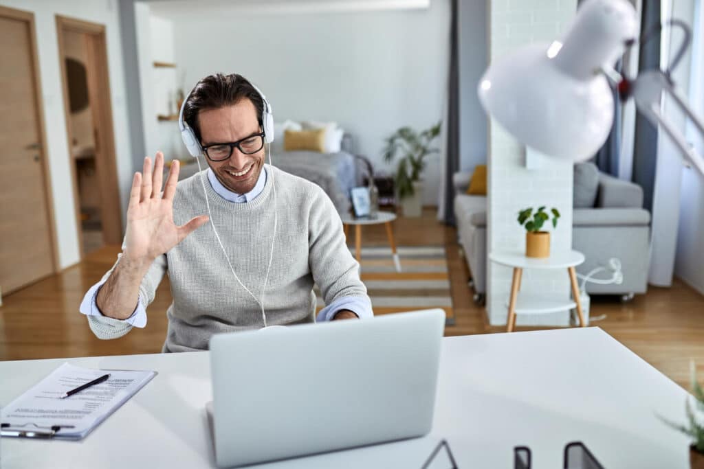 young happy businessman waving while having online meeting laptop from home